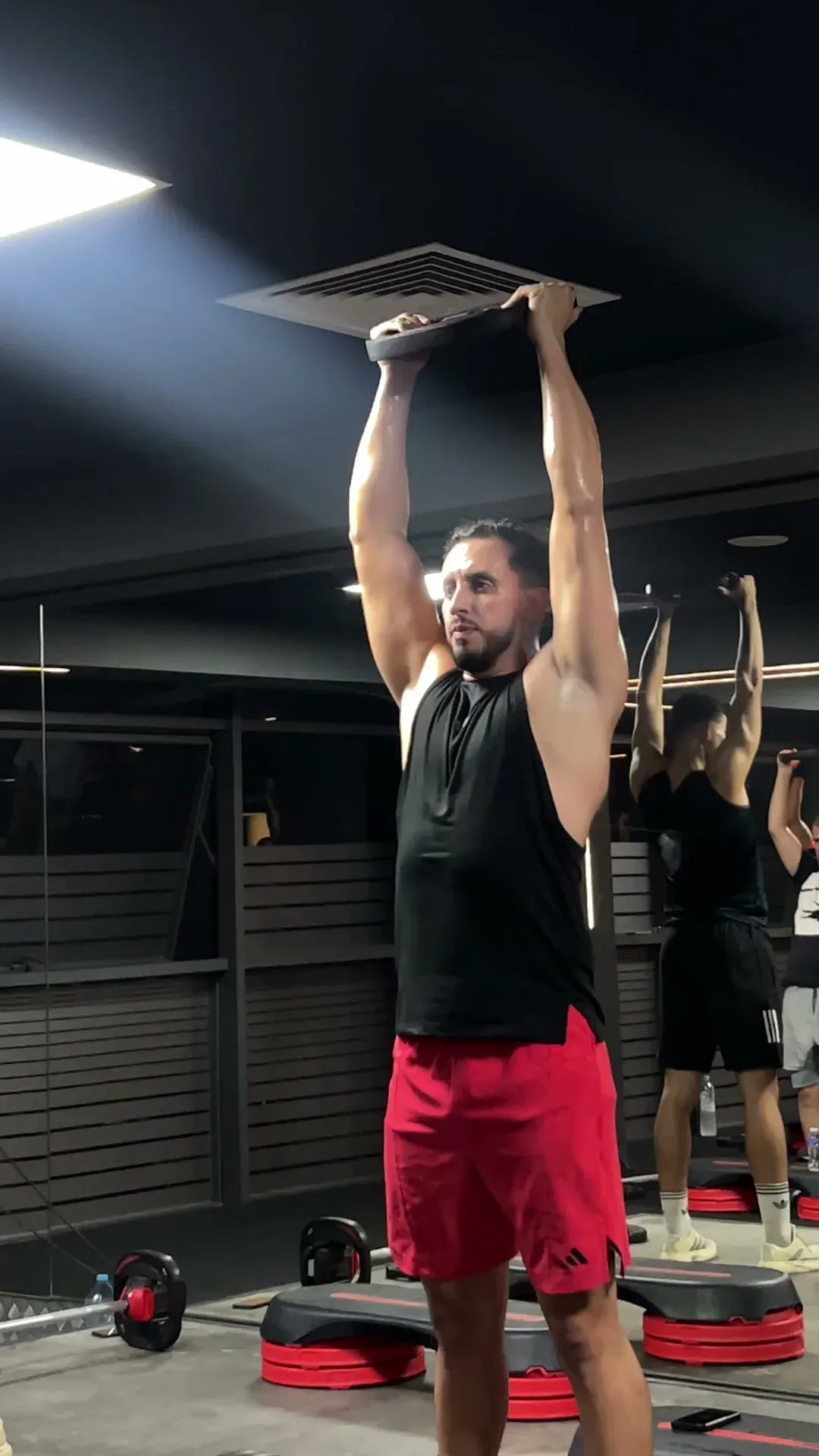 Cours de Body Pump : un adhérent porte des disques au-dessus de la tête