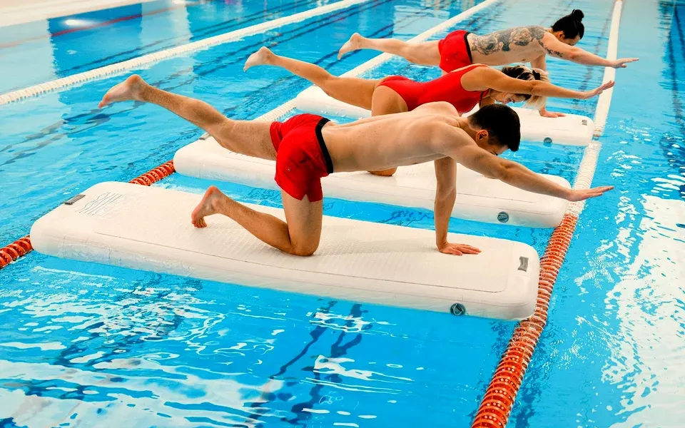 Trois personnes s’entraînent sur des plateformes flottantes dans une piscine intérieure