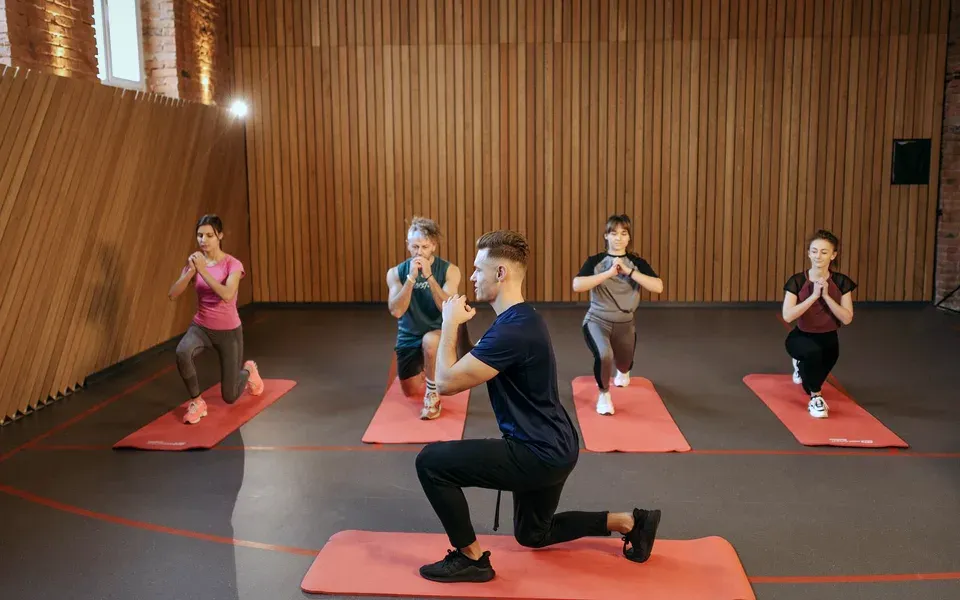 Un coach et quatre élèves en fente sur des tapis rouges dans un studio aux murs en bois