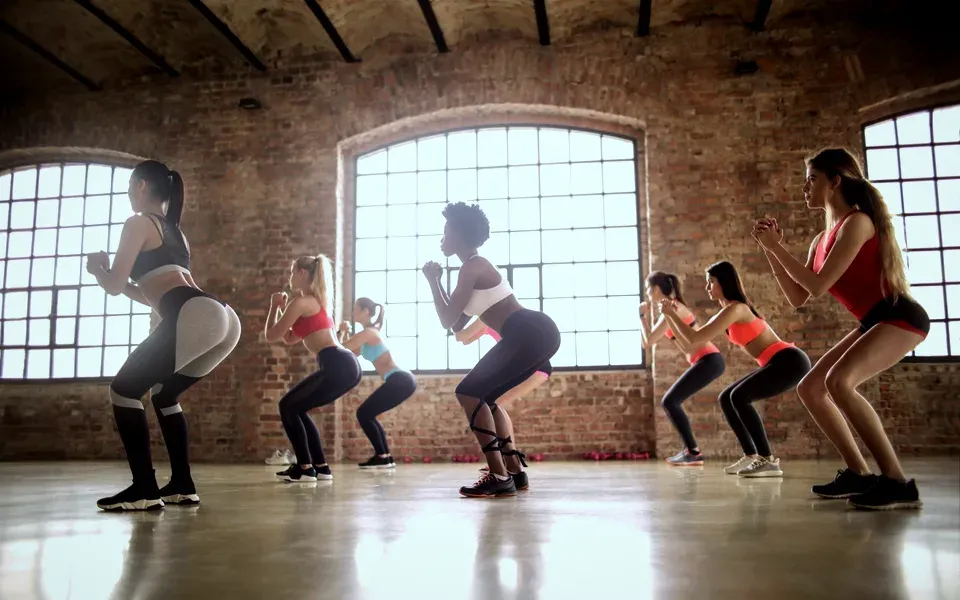 Un groupe fait des squats avec élastiques dans un studio aux murs de briques