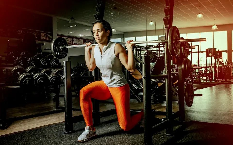 Une femme fait un squat avec barre dans une salle de musculation