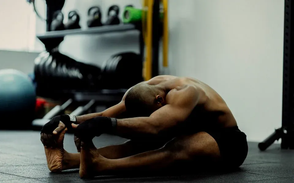 Un sportif s’étire assis, jambes tendues, dans une salle de musculation