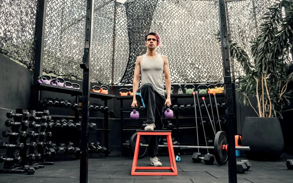 Un homme monte sur une boîte avec deux kettlebells