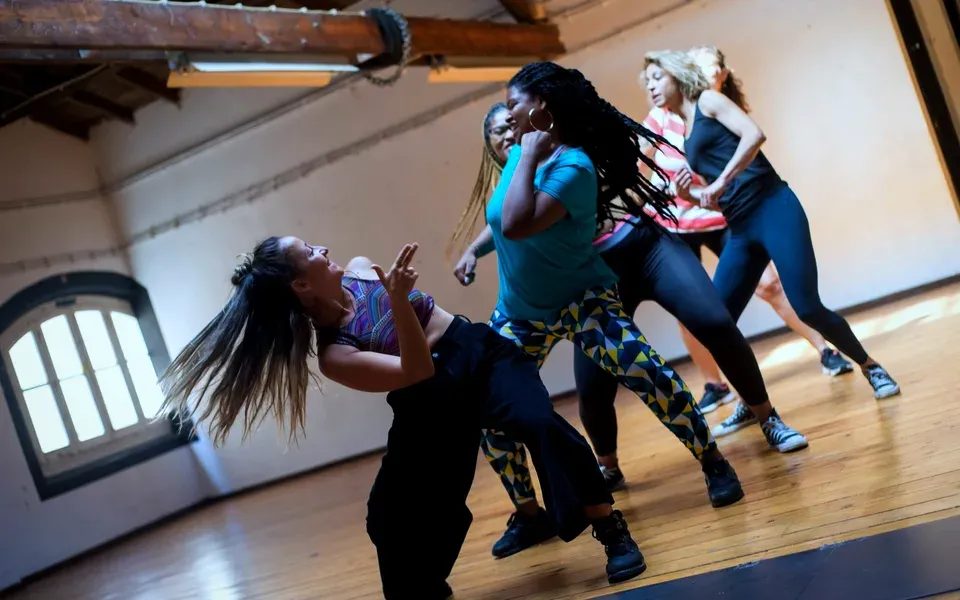 Un groupe danse dans un studio avec poutres et grandes fenêtres