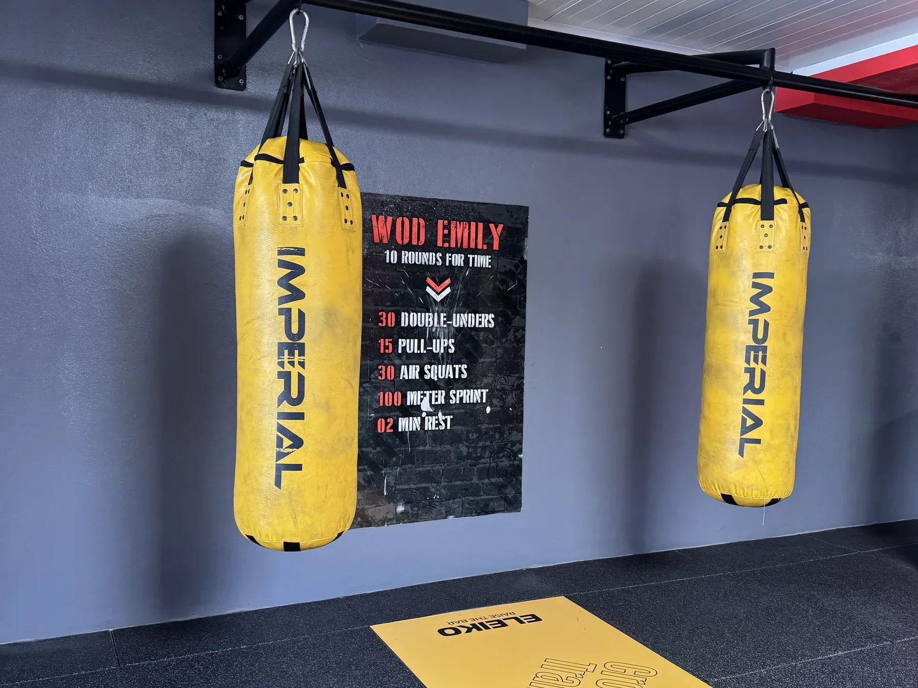 Deux sacs de frappe jaunes, tableau d’entraînement WOD et tapis Elite Cross Training