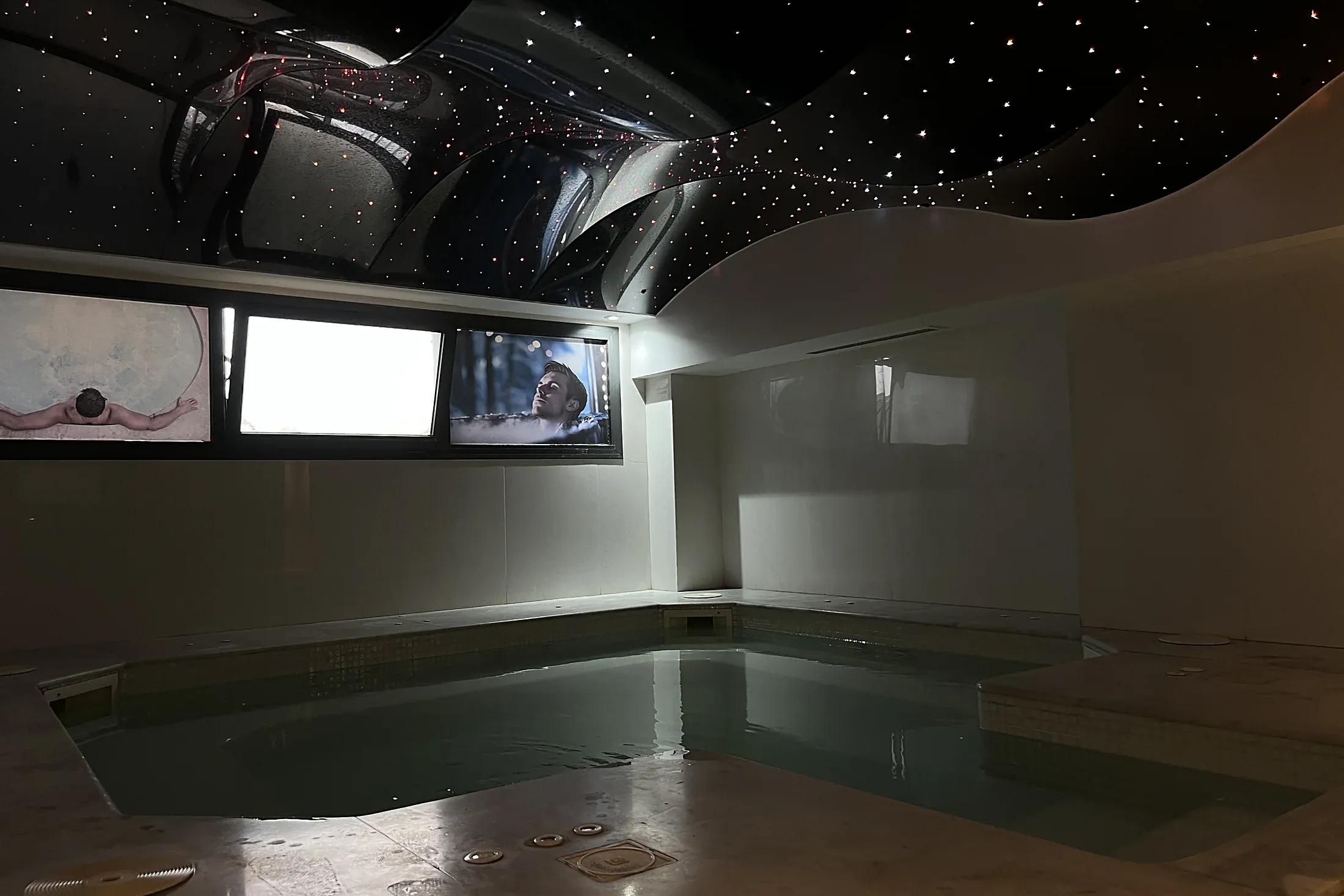 Jacuzzi sous un plafond étoilé, avec trois écrans au-dessus du bassin